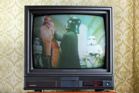 A photo of Darth Vader choking someone on a retro TV set.